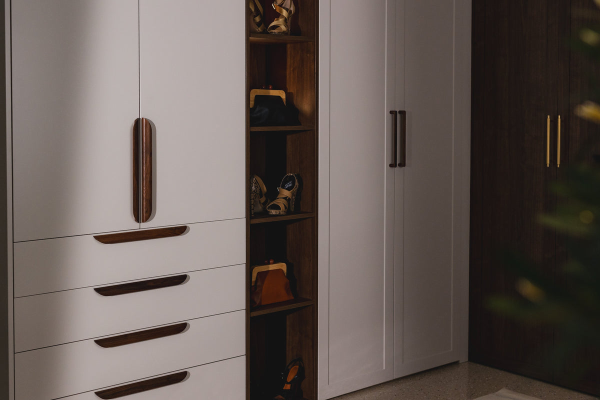 Floor-to-ceiling wardrobe with pale grey doors, drawer fronts with long timber pull handles and a lit open timber shelf unit