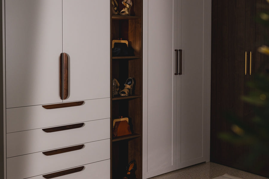 Floor-to-ceiling wardrobe with pale grey doors, drawer fronts with long timber pull handles and a lit open timber shelf unit