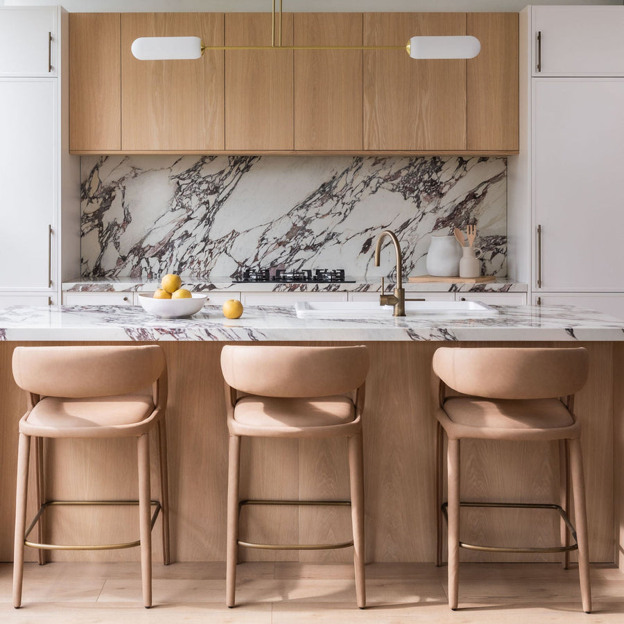 Two-tone kitchen in the Customea display with timber-look wall cabinets, white tall doors, a marble splashback and an island with three stools