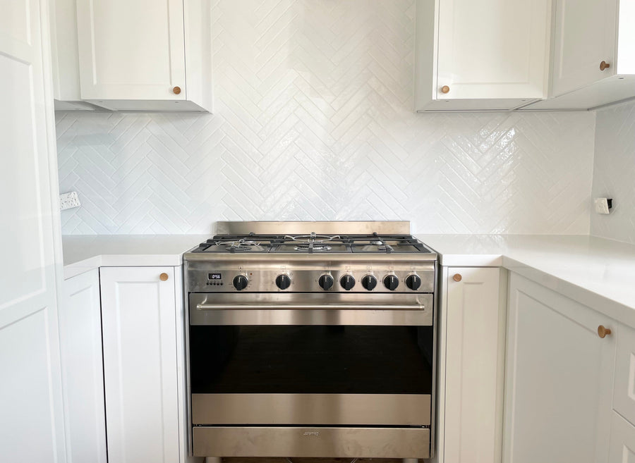 White French Shaker kitchen doors with round knobs around a freestanding stainless steel oven and herringbone tiled splashback