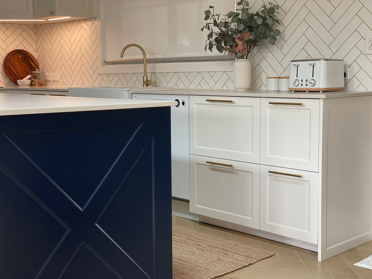 Kitchen with white French Shaker doors and drawer fronts beside a navy island panel with a cross design