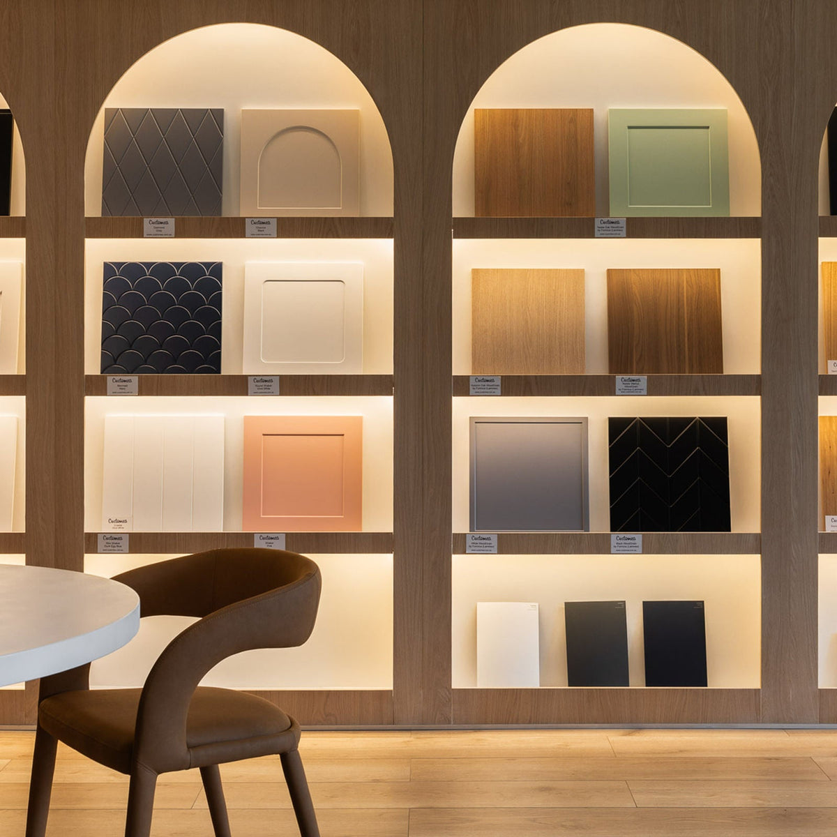 Full-size door samples in painted, timber-look and patterned finishes displayed on lit arched shelves in the Customea showroom